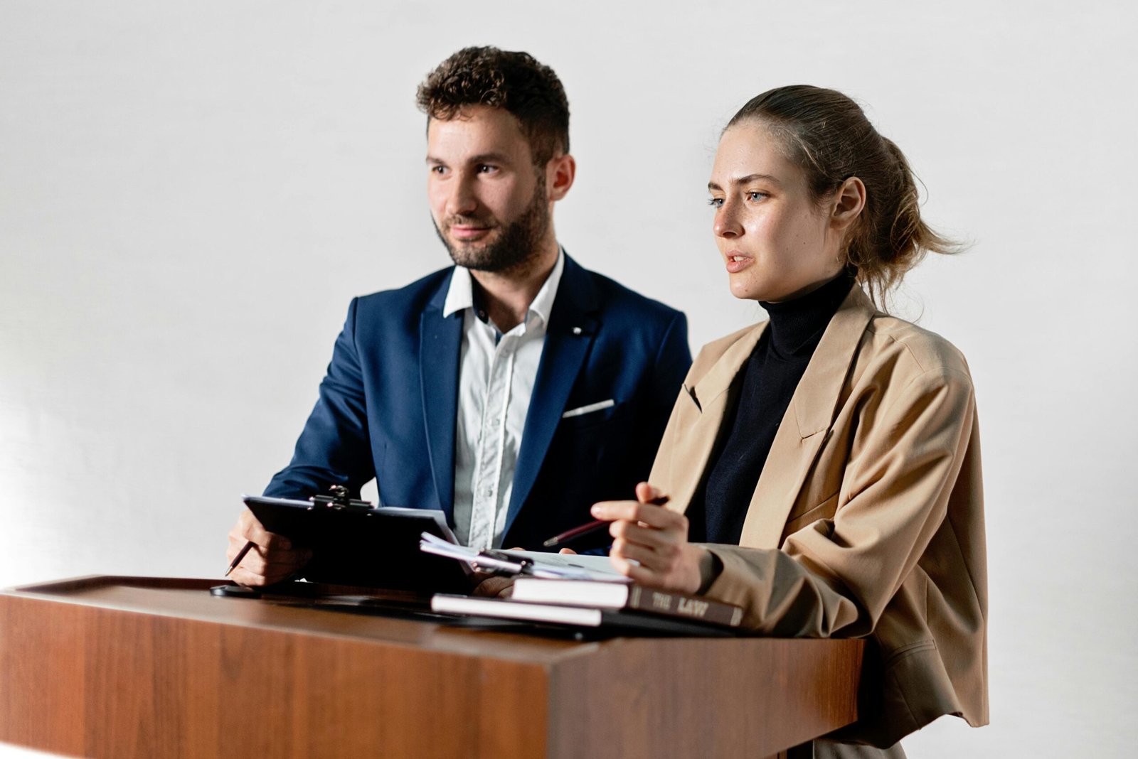 Two adults in formal attire are discussing documents at a podium indoors.