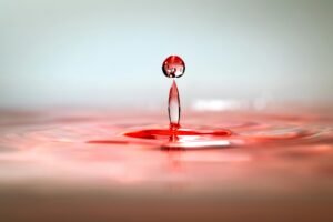 Dynamic close-up of a red water droplet captured in motion with ripples on the surface.