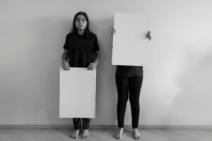 Two women holding blank cardboard signs in a minimalist setting, São Paulo.