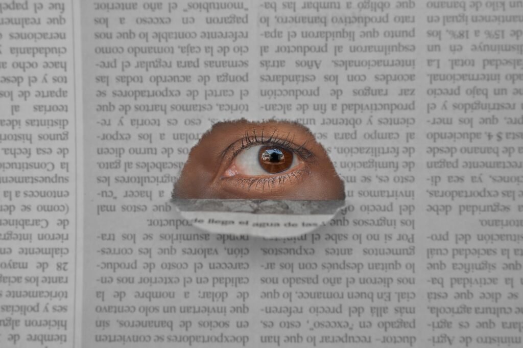 Artistic image of an eye peering through a hole in a newspaper, symbolizing insight and observation.